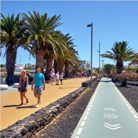 Costa Teguise seafront promenade in Lanzarote with palm trees, walkers and a dedicated cycle lane along the Atlantic